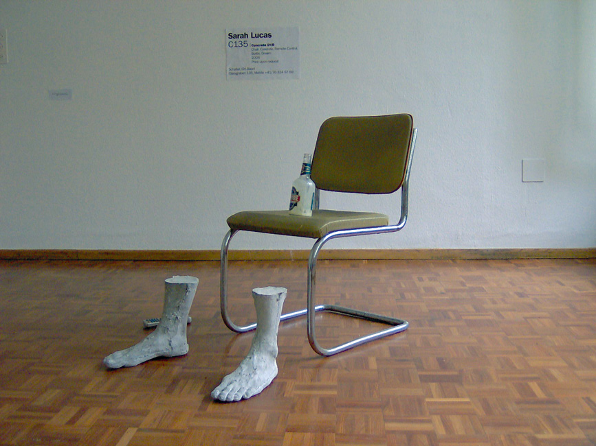 Installation (Stuhl, Beton, DVD-Fernbedienung, Bierflasche, Rahm, Legende)
